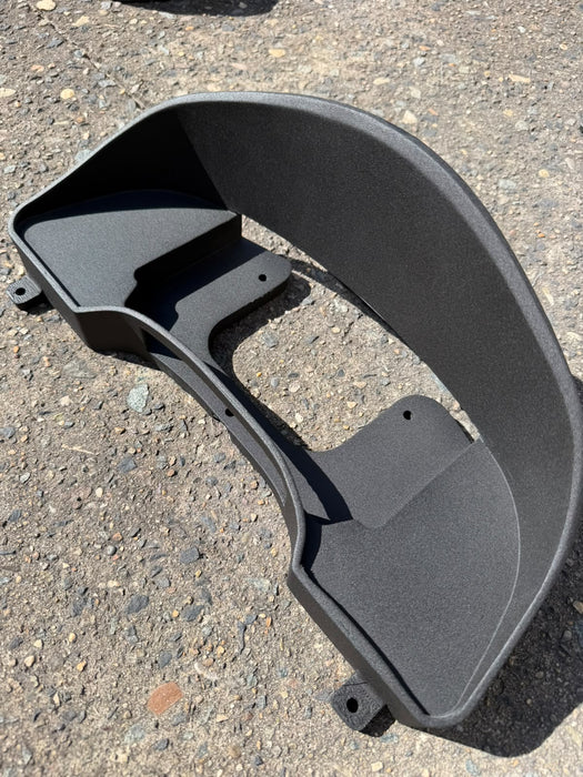 A black molded plastic automotive part, likely a fender or wheel arch trim piece, photographed outdoors on a gravel surface.