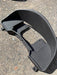 A black molded plastic automotive part, likely a fender or wheel arch trim piece, photographed outdoors on a gravel surface.